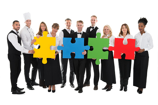 Portrait of confident restaurant staff joining jigsaw pieces against white background