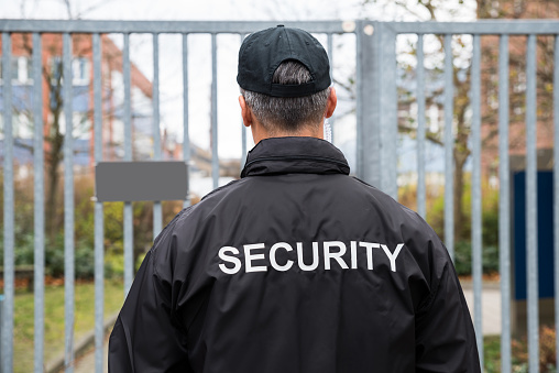Rear view of mature security guard standing in front of gate