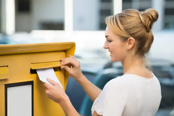 Happy young woman inserting letter in mailbox