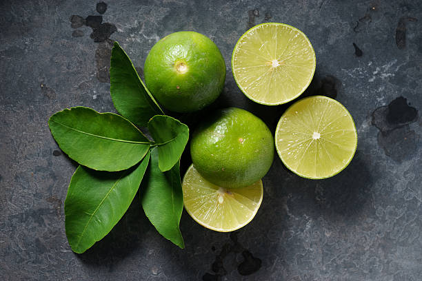 limas frescas sobre fondo oscuro - limones verdes fotografías e imágenes de stock
