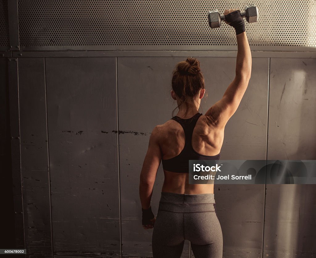 Woman Lifting Weights A strong and fit woman with her back to the camera lifting a weight above her head (stock image). Shoulder Stock Photo