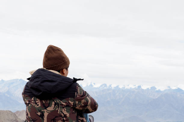 Young male traveler sitting on the sand cliff, thinking about something in Leh, Ladakh, India
