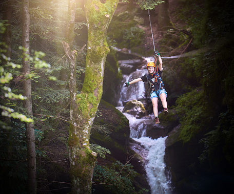woman smiling on tyrolean traverse with her arm raised, enjoying the adventure and feeling energic and happy.