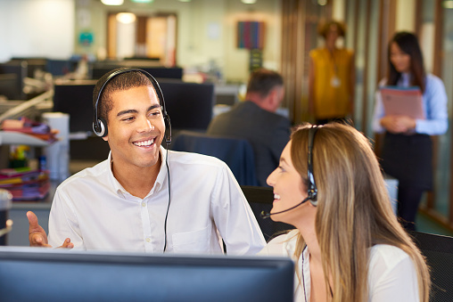 Portrait o female customer support or sales agent working in row with her colleagues at call center office. Business, technology, internet and network concept.