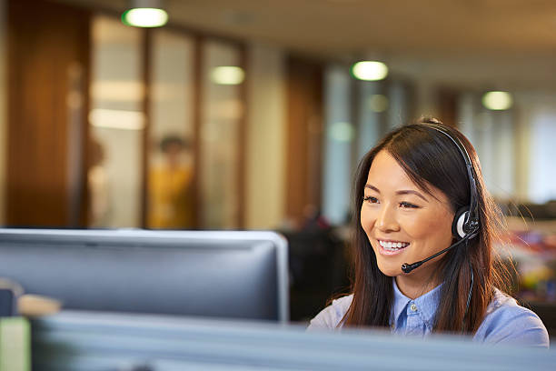 pleasure speaking with you a young call centre representative greets a caller in a large open plan office . Co-workers can be seen defocussed in the background . headset stock pictures, royalty-free photos & images