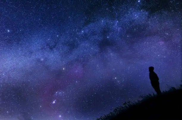Silhouette of a man looking at the stars on a hill.