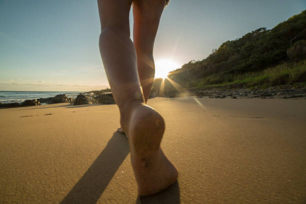 istock Low angle view of barefeet walking on beach at sunrise 600701334