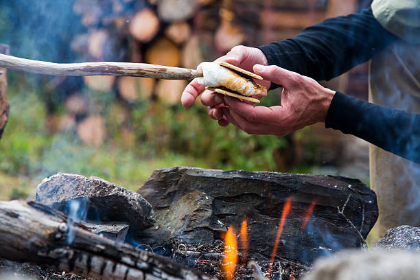 Hands making Smores with marshmallow and chocolate over campfire