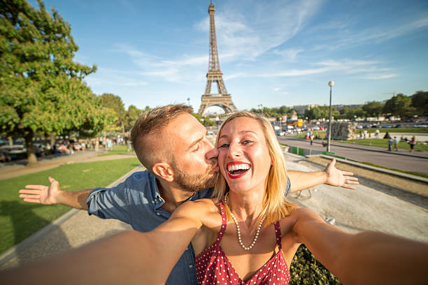 Self portrait of young couple at the Eiffel tower, Paris Cheerful young couple in Paris in front of the Eiffel tower take a selfie while kissing. Sunset in summertime. paris france eiffel tower love kissing stock pictures, royalty-free photos & images