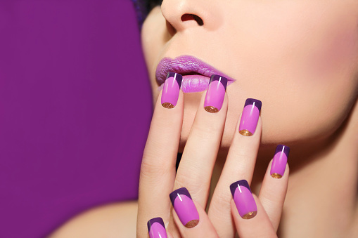 Mauve lip and French manicure with gold glitter on a purple background.