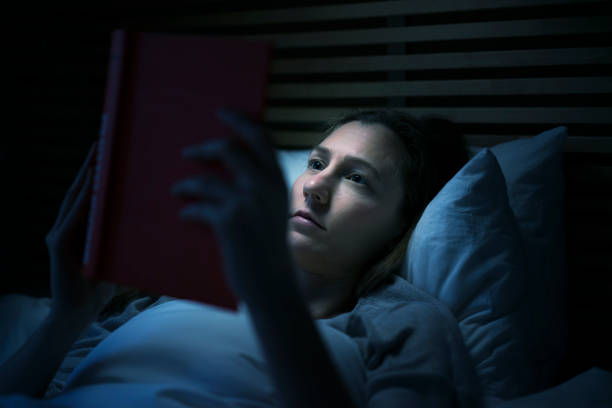 istock Woman reading a book in bed at night 600994448