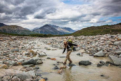 Female Backpacker balancing on rocks, crossing river in Wilderness Area, Alaska