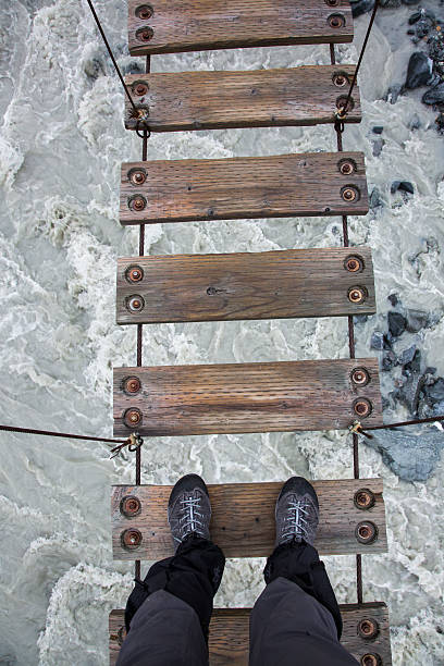 Looking Down at Feet on Dangerous Wooden Footbridge with River and Rocks below