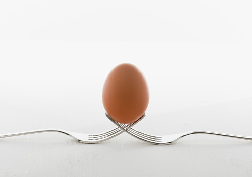 egg in balance on two forks with white wooden kitchen table and space for text. whit background