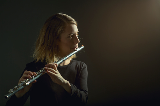 A lovely young flutist performing under stage lights with copy space to her right (stock image)