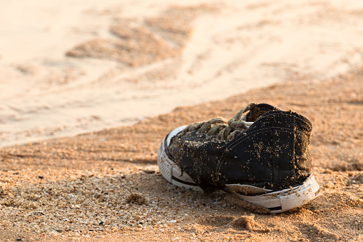 Old black sneakers abandoned on the sand at the beach
