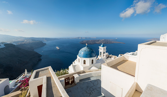 Early morning view in Santorini of the Imerovigli church sitting on top of the volcanic caldera. Santorini in Greece is one of the most famous travel destination in the World with numerous cruise ships anchoring in the bay below. The architecture is also famous for the duotone colors of the white painted buildings and light blue details.