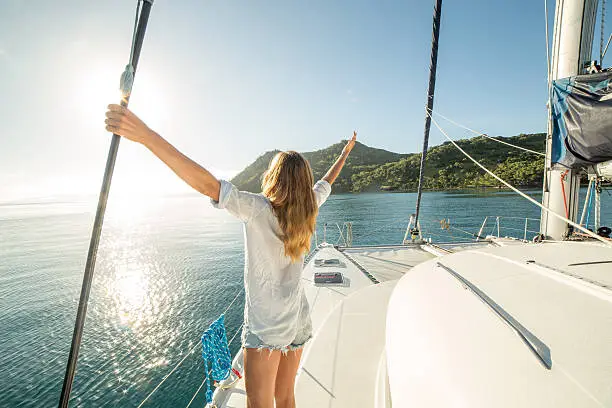 Happy young woman on a sailing boat arms outstretched for freedom and positive emotions. 
