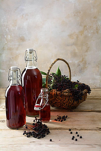 bottles with the red juice from black elderberries (Sambucus nigra) bottles with the red juice from black elderberries (Sambucus nigra) and a basket with berries on rustic wood planks in front of a vintage wall with copy space, vertical, selected focus autumn copy space rural scene curing stock pictures, royalty-free photos & images