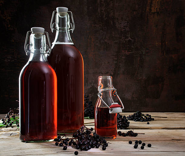 bottles with red juice of black elderberries (Sambucus nigra) an bottles with red juice of black elderberries (Sambucus nigra) and some berries on rustic wooden planks, dark background with copy space autumn copy space rural scene curing stock pictures, royalty-free photos & images