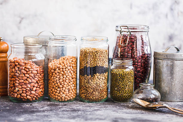 Superfoods meals. Collection of grain products, lentils, peas, soybeans and red beans in storage jars over on kitchen rural table. Vegetarian products.  bean stock pictures, royalty-free photos & images