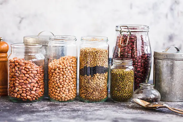 Collection of grain products, lentils, peas, soybeans and red beans in storage jars over on kitchen rural table. Vegetarian products. 