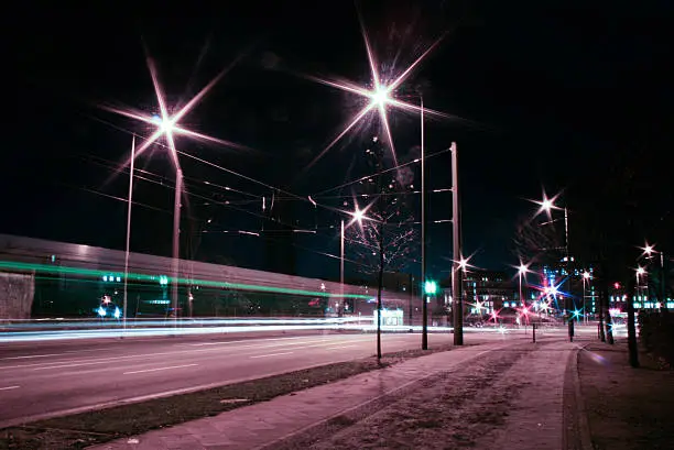 Urban night scene, long exposure. A tram is driving by, streetlights are red and green and a sidewalk is in the foreground