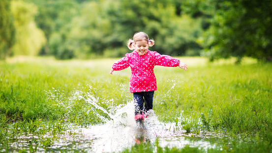 happy child girl running and jumping in puddles after rain in summer