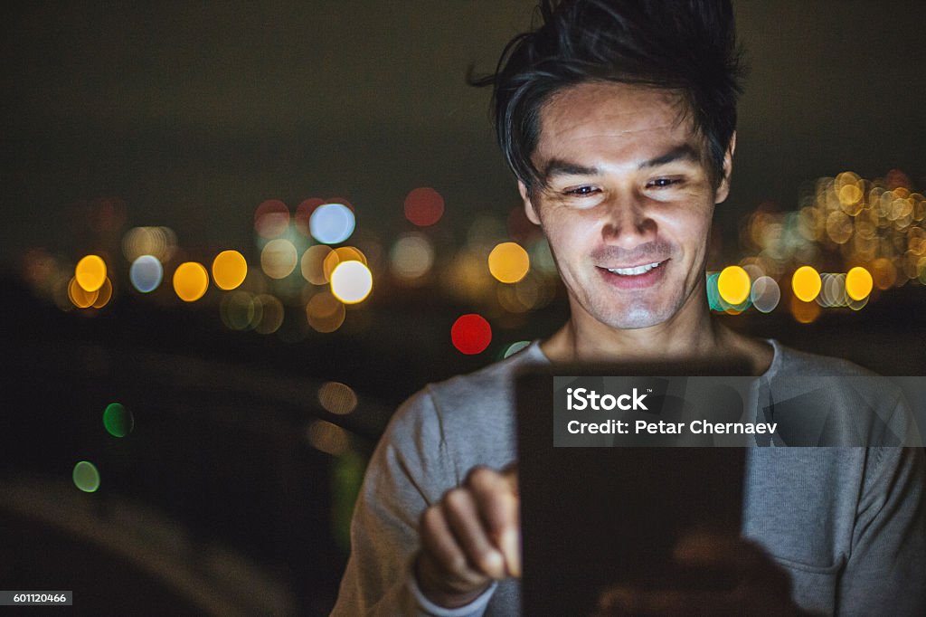 Communication at night Young man with digital tablet outdoors at night, with copy space and city lights in the background, with copy space. Night Stock Photo