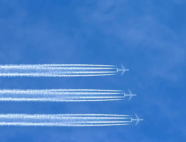 three airplanes leaving horizontal traces on a clear blue sky.