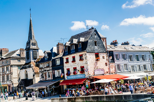 Honfleur, France - July 25, 2016: Tourists outside the cafe La Maison Bleue on Quai Saint Etienne at the harbour in the town of Honfleur in the Normandy region of France. The town was a favourite of many artists, and of the musician Erik Satie, and nowadays enjoys a thriving summer tourist industry, attracted by its open air markets, its culture, cafes and period architecture.