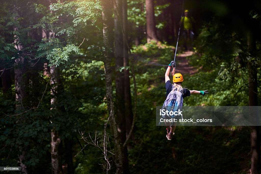 fun, adrenaline and adventure on the zip line rear view of woman in the forest with her backpacker enjoying adventure on tyrolean traverse. Zip Line Stock Photo