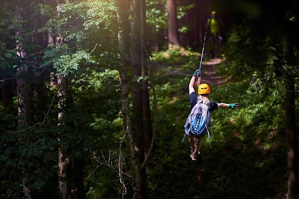 fun, adrenaline and adventure on the zip line rear view of woman in the forest with her backpacker enjoying adventure on tyrolean traverse. zip line stock pictures, royalty-free photos & images