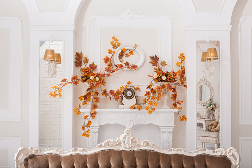 Yellow leaves entwined wall of white hall with decorative classical fireplace and mirrors