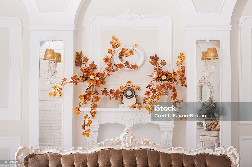 Yellow leaves entwined wall of white hall with fireplace Yellow leaves entwined wall of white hall with decorative classical fireplace and mirrors Autumn Stock Photo