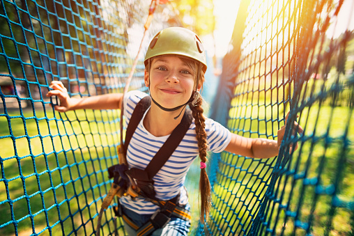 Little girl in ropes course in outdoors adventure park. The girl aged 10 smiling at the camera and walking in a safety net obstacle,