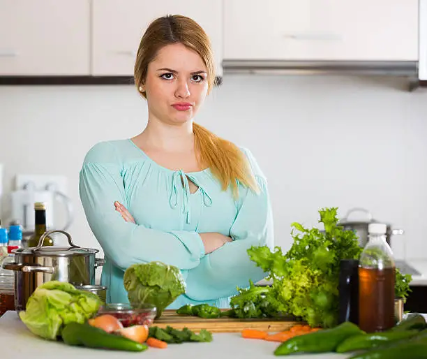 Photo of Young housewife tired of cooking vegetables in domestic kitchen
