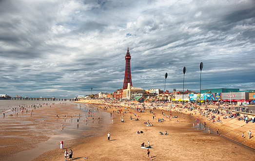 Blackpool, United Kingdom - August 6, 2016: Blackpool's famous Golden Mile beach. People sunbathing in the beach. Blackpool Tower in the background. HDR.