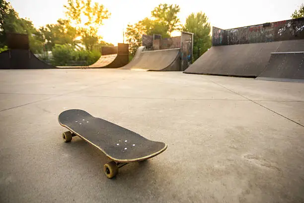 Wide angle of a skate park during sunset with skateboard in focus.