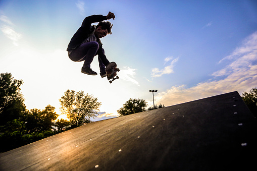 Silhouette of a young skater jumping with skateboard at a skate park at sunset. About 25 years old, Caucasian male.
