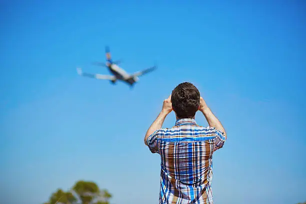 Man is looking at the glide path and landing plane or taking a photo of it. Aircraft spotting concept