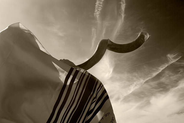 Jewish man blowing the Shofar in Yom Kippur Jewish man wearing Talit (praying shawl) and blowing the Shofar against sky. Toned image. jewish prayer shawl stock pictures, royalty-free photos & images