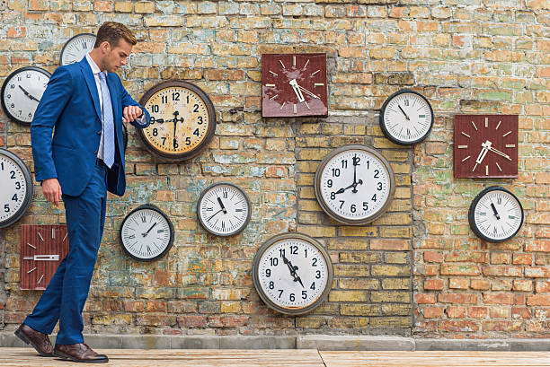 istock Man in suit standing near wall with clocks 601361978