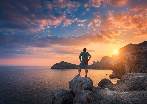 istock Young standing man with backpack on the stone at sunset 601362038