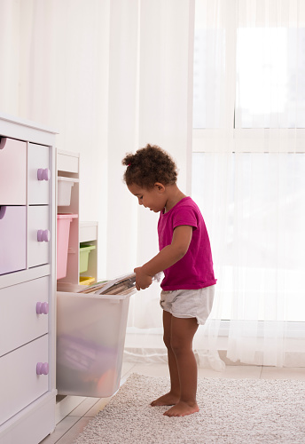 Mixed race girl opening drawer, pulling out books and puzzle toys.