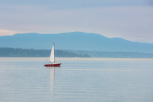 Red sailboat sailing in calm blue bay