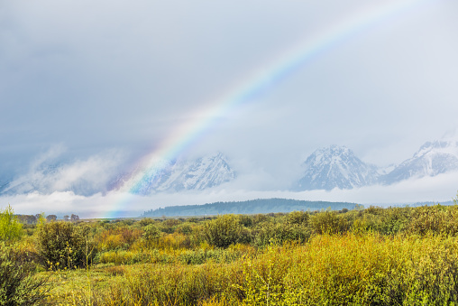 Grand Teton mountains covered with fog and dark storm clouds with rainbow