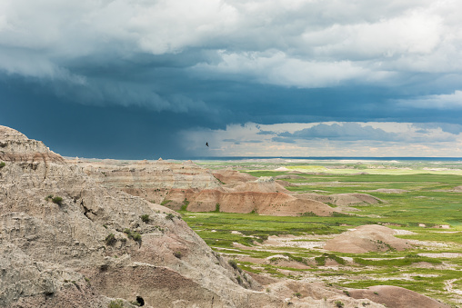 Dark blue storm clouds and bird in Badlands National Park with prairie valley view