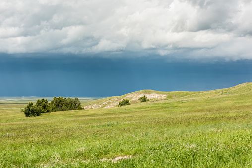 Dark blue rain storm clouds contrast with green prairie steppe grass valley in Badlands National Park