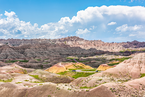 Landscape view of Badlands National Park with green plants and curved road with cars and clouds